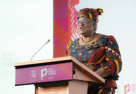 Oratrice au Forum public de l'OMC 2024 devant un podium lors de la session sur la ré-globalisation.