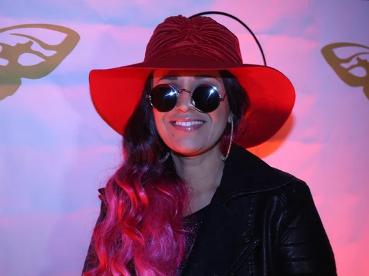 Lââm posant sous un éclairage rose, arborant un chapeau rouge et des lunettes rondes.