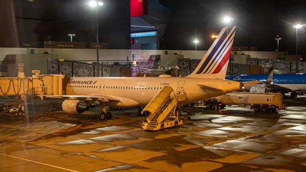 Un Airbus A320-111 d'Air France à quai la nuit, connecté à une passerelle d'embarquement