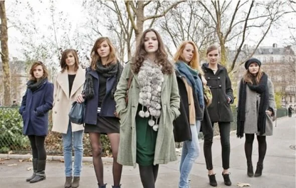 Ces jeunes Parisiennes posent en ligne sur un chemin pavé, arborant divers manteaux d'hiver et écharpes.