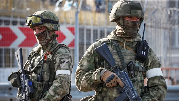 Un groupe de soldats courant en formation sur une aire pavée, avec de la fumée orange en arrière-plan.
