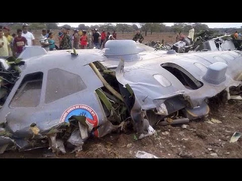 Épaves d'un avion militaire sur un sol terreux, avec des témoins à l'arrière.