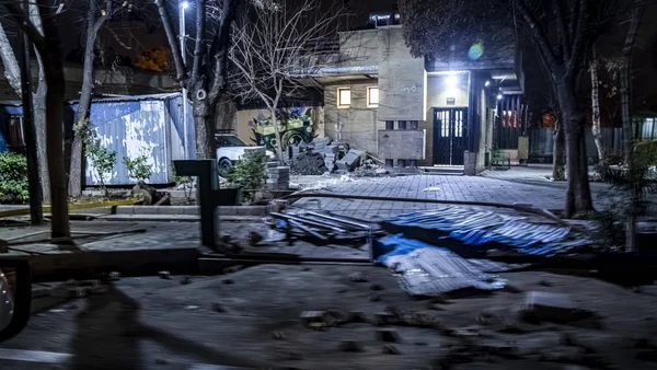 Scène nocturne de zone résidentielle endommagée avec des débris au sol.
