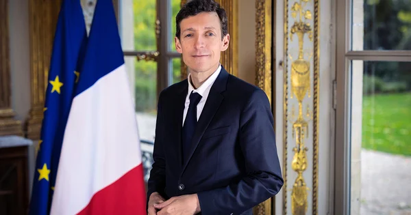 Le ministre de l'Éducation nationale en costume devant les drapeaux français et européens.
