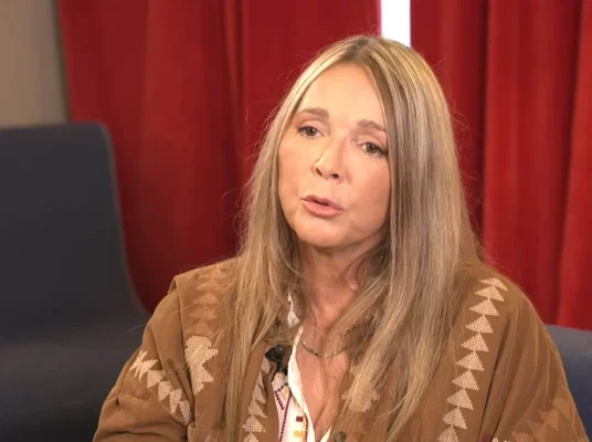 Hélène Rollès lors d'une interview, assise devant un fond de rideau rouge.