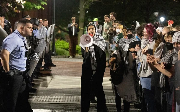 Manifestation nocturne sur le campus de Penn : un manifestant au mégaphone face à des policiers anti-émeute.