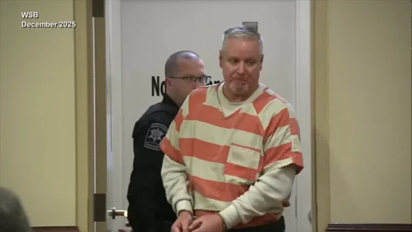 Colin Gray en tenue de prisonnier escorté par un agent des forces de l'ordre.