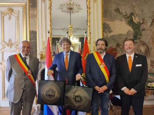 Hommes en costume officiel posant avec des sacs noirs lors d'une visite.