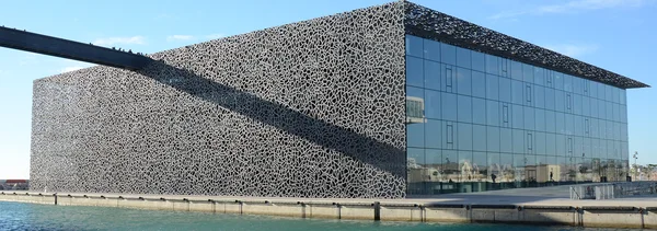 La façade perforée caractéristique du Mucem au bord de l'eau, avec la passerelle en premier plan.