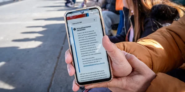 Un smartphone affichant un avis en espagnol sur l'application CBP One, tenu par une personne dans la rue.