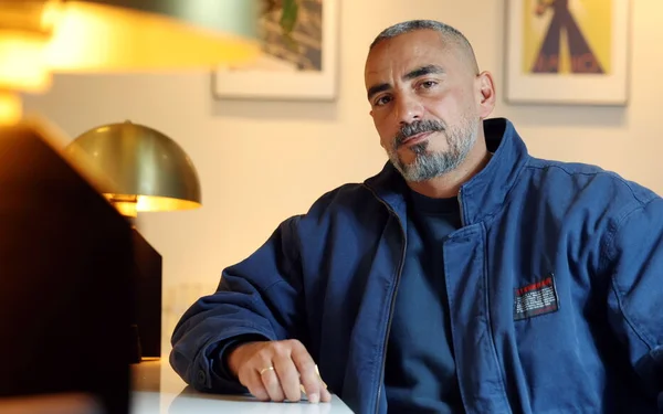 Julien Mairesse en mars 2025, assis dans un intérieur décoré d'un tableau encadré et d'une lampe.