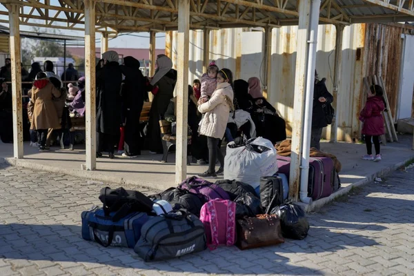 Réfugiés syriens en attente avec leurs bagages sous un abri métallique.