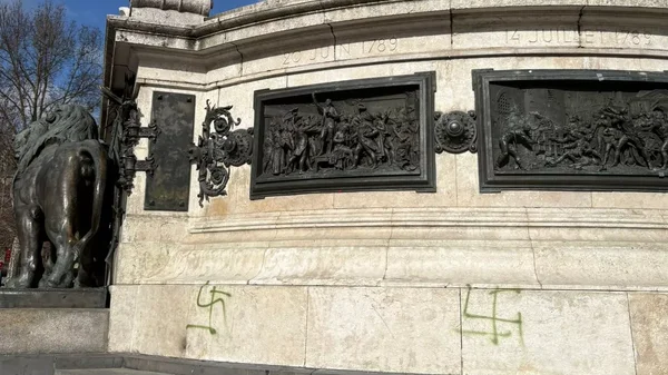 Détail du bas du monument montrant un lion de bronze, des dates historiques et des tags.