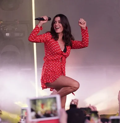 Jenifer en robe rouge à pois en pleine performance scénique énergique.