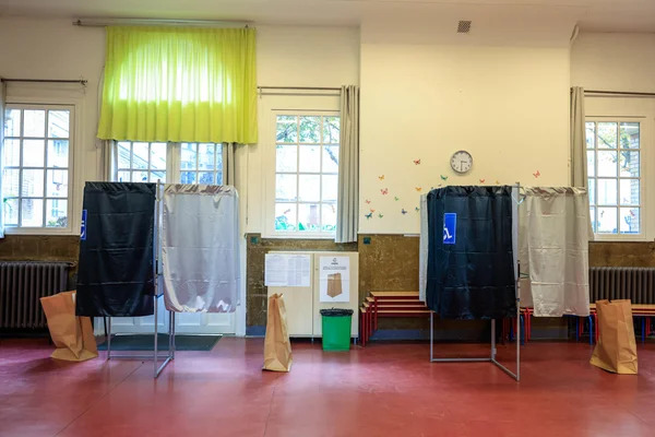 Intérieur d'un bureau de vote avec plusieurs isoloirs et des bancs.