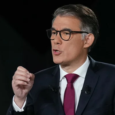 Olivier Faure en costume et cravate magenta, en pleine discussion et gesticulant de la main.