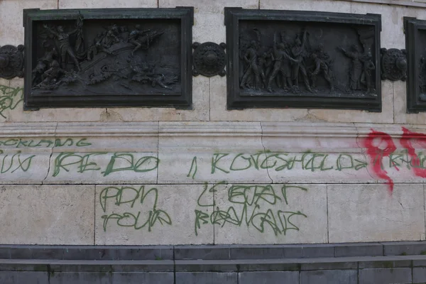 Bas du monument avec panneaux en bronze et graffiti incluant « REDO » et « POUR RENAGATS ».