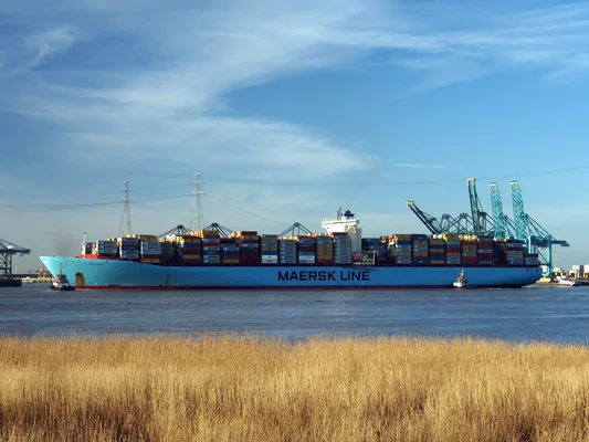 Le navire Emma Maersk navigue sur l'eau, chargé de conteneurs, avec des grues en arrière-plan.