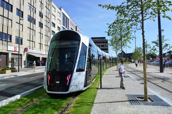 Un tramway moderne traversant une ville avec des passants sur le quai.
