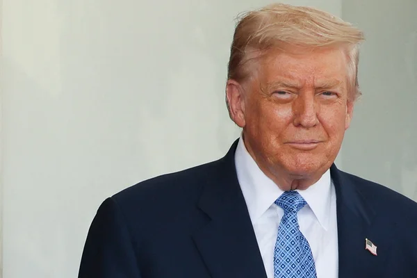Un homme en costume avec une cravate bleue et une broche drapeau américain sur le revers.