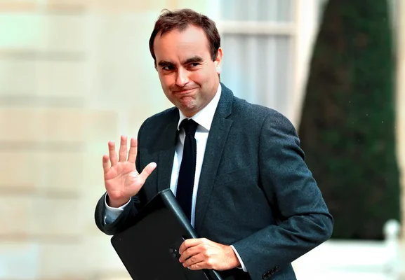 Sébastien Lecornu tient un dossier et fait un signe de la main.