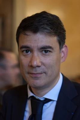 Olivier Faure, député de Seine-et-Marne, posant en costume et chemise claire sur fond intérieur flou.