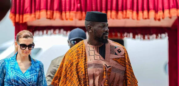 Une personne en tenue traditionnelle guinéenne est assise en tenant un drapeau.