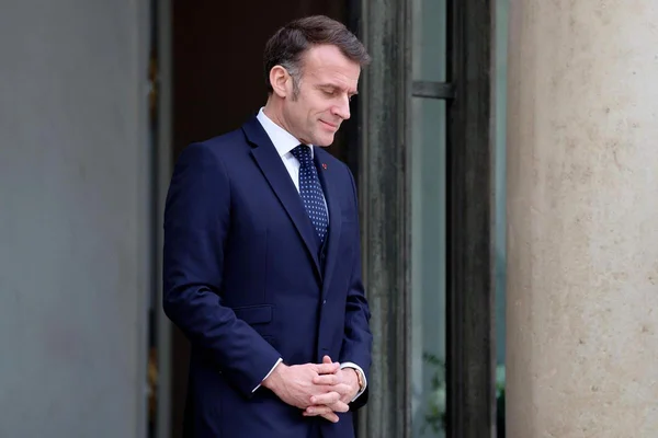 Emmanuel Macron en costume bleu marine, les mains croisées.