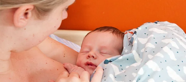 Une femme tenant un nouveau-né emmailloté dans une couverture bleue, symbole de la prévention de la transmission mère-enfant.