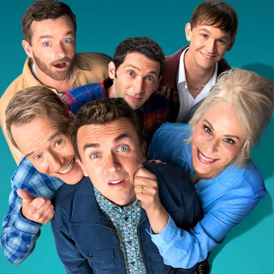 Photo de groupe officielle avec le casting disposé en cercle autour du personnage central en veste bleue.