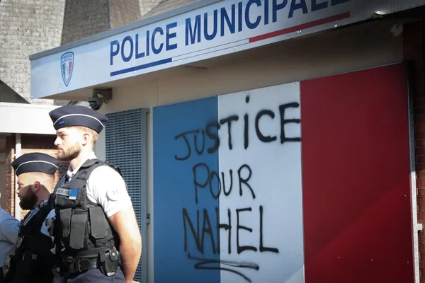 Policiers en uniforme devant un panneau 'Police Municipale' tagué.