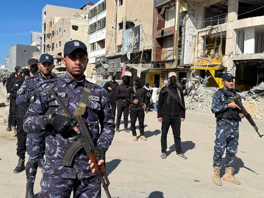 Des policiers armés en tenue de camouflage dans une rue de Gaza aux bâtiments endommagés.