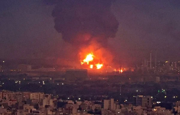 Une raffinerie de pétrole en feu à Téhéran, dégageant une épaisse fumée noire au-dessus de la ville.