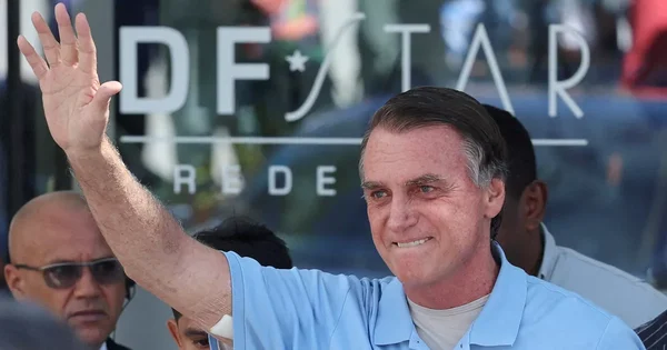 Un homme en polo bleu clair saluant devant une paroi en verre.