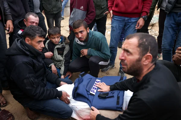 Des hommes debout devant une dépouille couverte d'un gilet 'PRESS'.