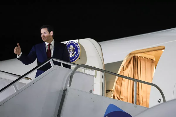 Marco Rubio faisant un pouce en haut devant son avion officiel la nuit.