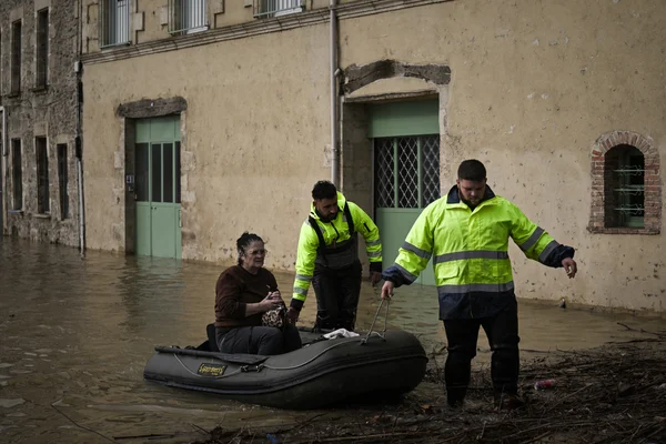 Des secouristes aident une femme âgée assise dans un canot gonflable à traverser une zone inondée.