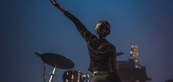 Participant au Festival PSPBB 2026, bras droit levé, devant un fond bleu et des instruments de musique aux Plateaux Sauvages.
