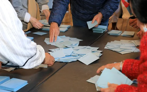 Bénévoles comptant ou organisant des documents électoraux, probablement des bulletins de vote, autour d'une table.
