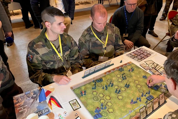 Militaires jouant à un jeu de guerre sur grille hexagonale avec des figurines lors d'une simulation stratégique.