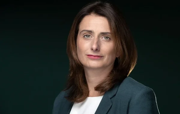 Marine Tondelier, portant un blazer sombre sur un fond vert.