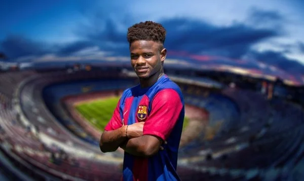 Joueur du FC Barcelone debout bras croisés devant un stade en arrière-plan flou.