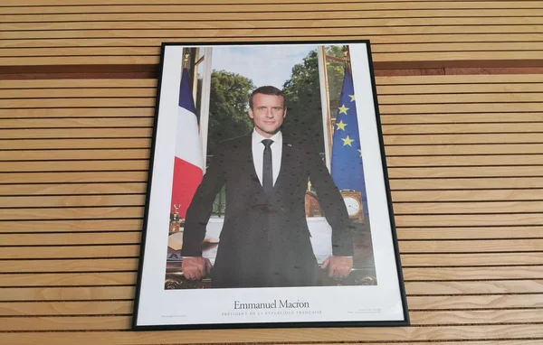 Le portrait officiel d'Emmanuel Macron debout devant son bureau et les drapeaux français et européen.