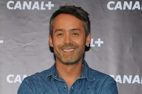 Yann Barthès en chemise en jean bleu souriant devant un fond aux logos CANAL+.