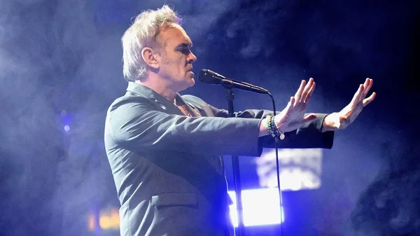 Morrissey performant sur scène lors d'un concert, vêtu d'un costume sombre et entouré de fumée.