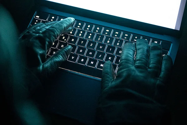 Des mains gantées de cuir noir saisissent des touches au clavier devant un écran lumineux.