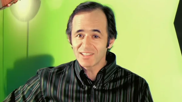 Jean-Jacques Goldman portrait torse nu, portant une chemise à rayures et souriant.