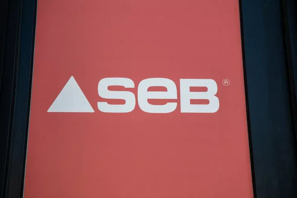 Logo graphique 'seb' en blanc sur fond rouge accompagné d'un triangle blanc.