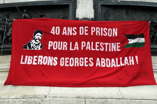 Banderoles de soutien à Georges Abdallah avec drapeau palestinien sur un mur en pierre.