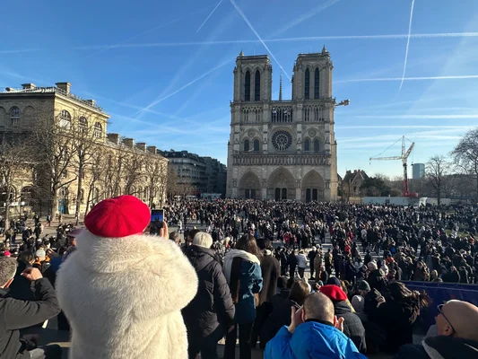 Foule de touristes devant la cathédrale Notre-Dame avec des grues de chantier en arrière-plan.